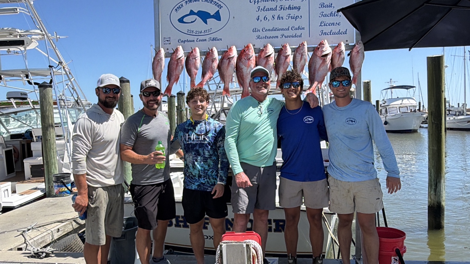 A group posing with a catch beside a boat